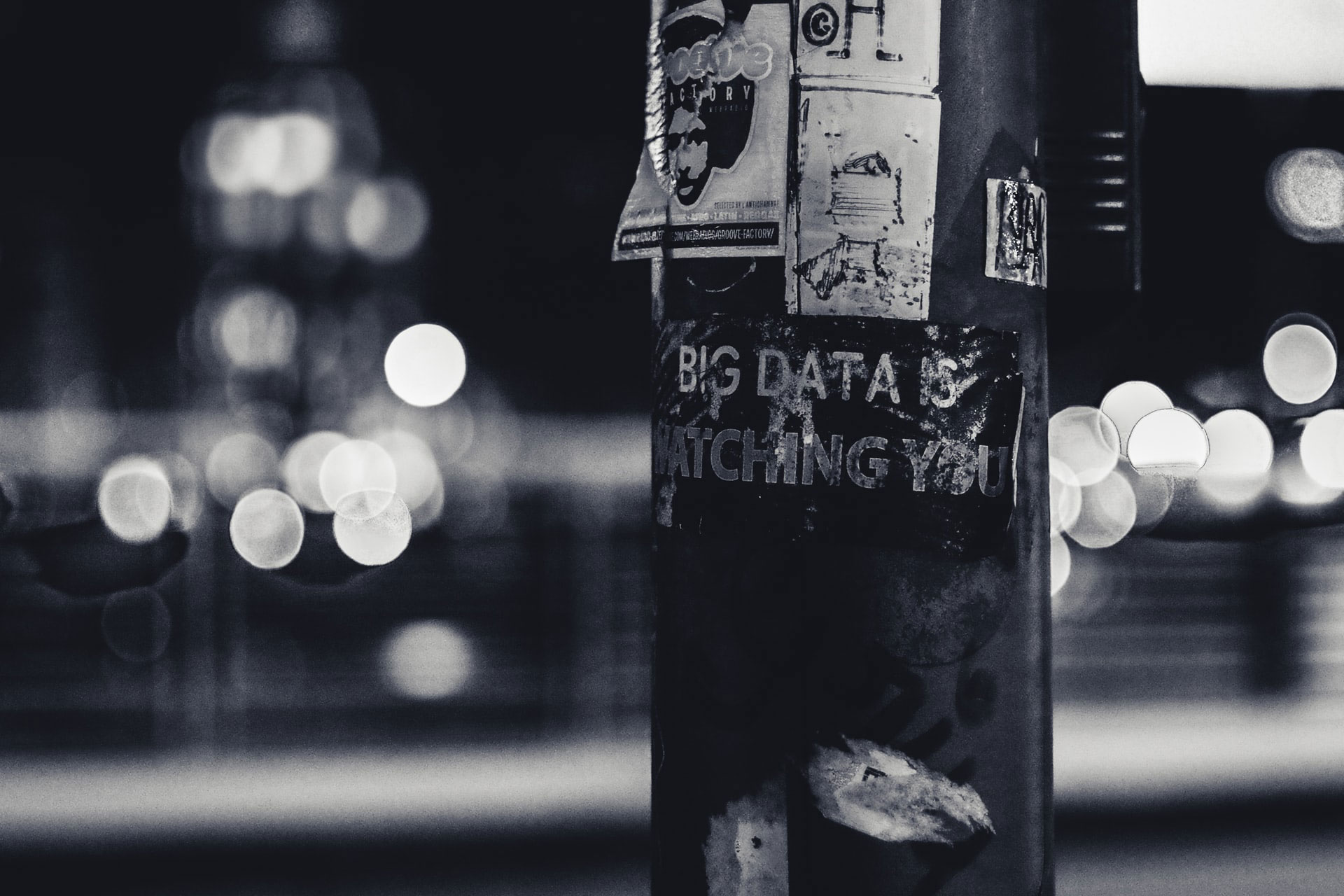 S/w-Foto eines Laternenpfahl auf dem neden einigen Aufklebern auch der Schriftzug "big data is watching you" steht © ev auf unsplash.com